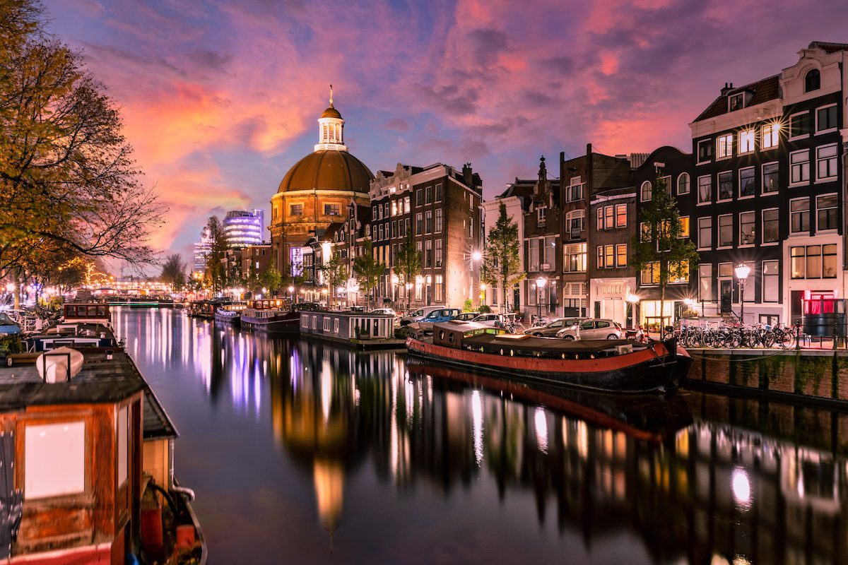 Scenic view of Amsterdam canal at sunset with historic buildings and boats reflecting on the water.