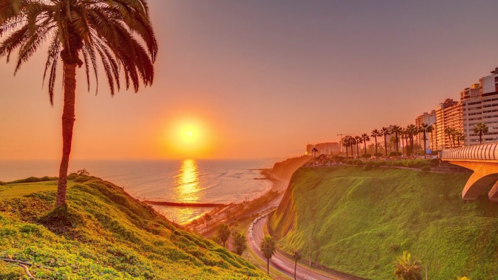 Aerial sunset view of Lima's Coastline in the neighborhood of Miraflores timelapse with orange light, Lima, Peru. Road with traffic and beach with ocean. Palm near Love park