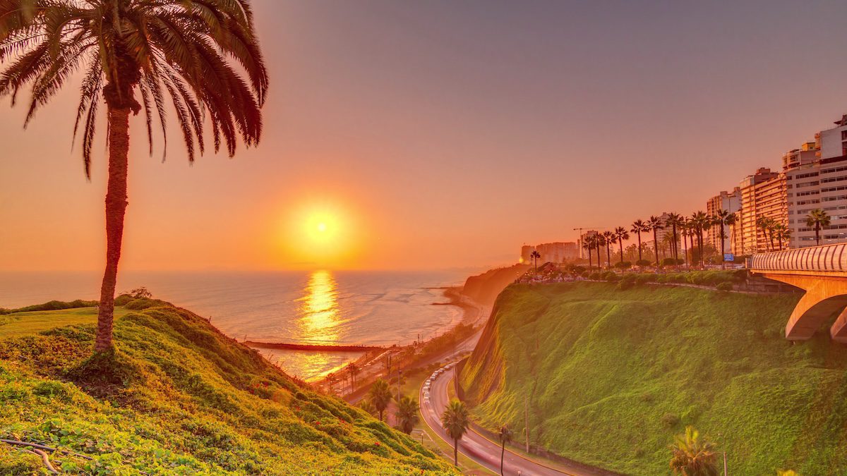 Aerial sunset view of Lima's Coastline in the neighborhood of Miraflores timelapse with orange light, Lima, Peru. Road with traffic and beach with ocean. Palm near Love park